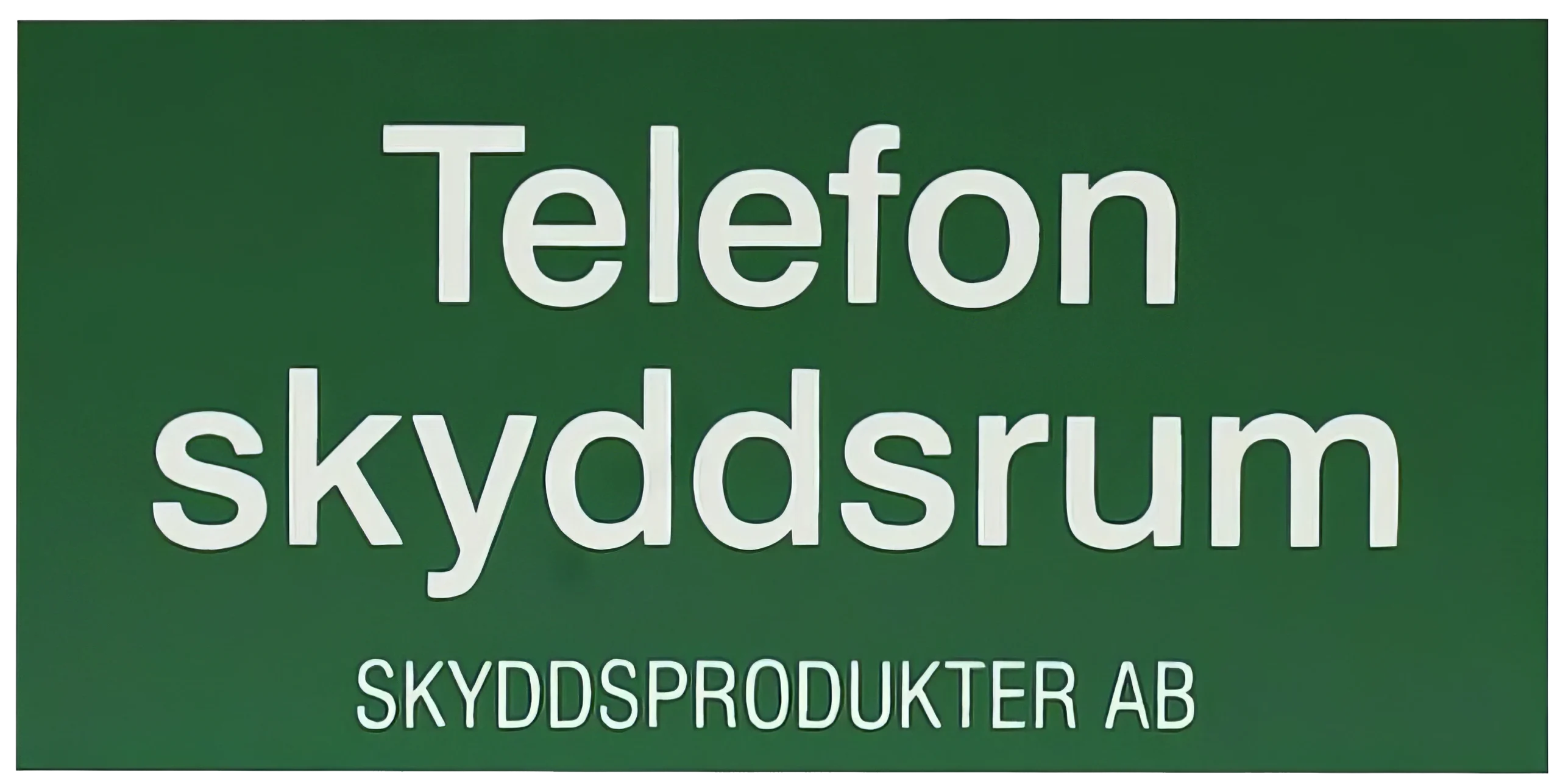 En grön skylt med vit text där det står ”Telefon skyddsrum” och nedanför, med mindre bokstäver, ”SKYDDSPRODUKTER AB.”.